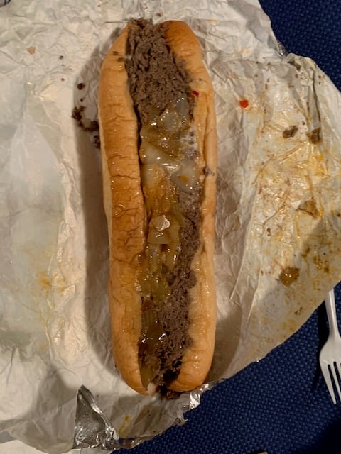 A cheesesteak sits on an opened wrapper, with flecks of onion visible
