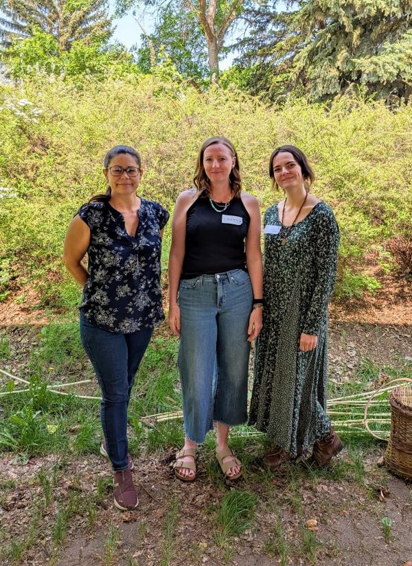 Three women standing in nature, volunteering at the Bark Harvesting Open Weave