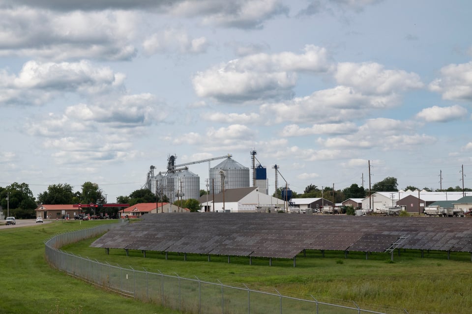 Solar farm with grain silos in the background.