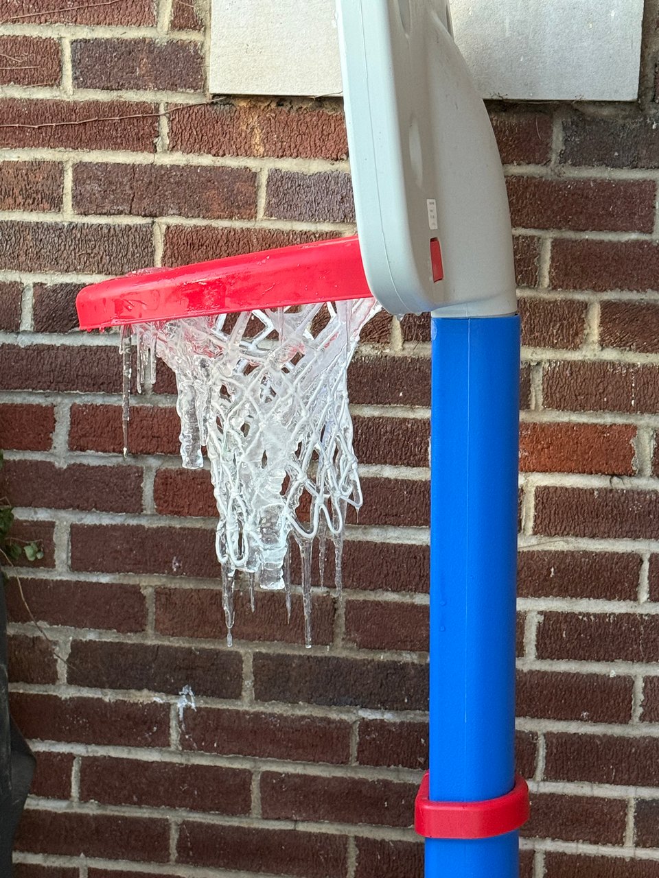 a little tykes basketball hoop, the net covered in ice with icicles hanging off of it