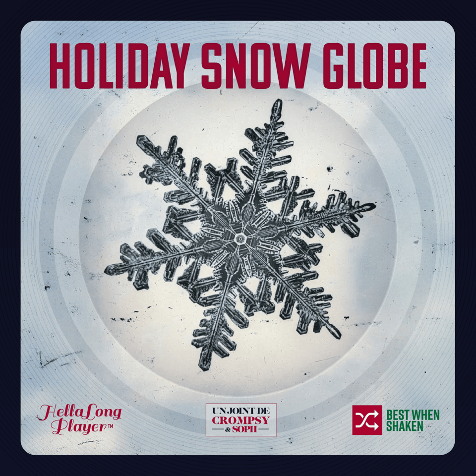 A microscopic photograph of an intricate snowflake crystal with symmetrical branching arms is displayed within a circular glass snow globe. The snowflake appears dark grey against a pale background with subtle radial textures. The image is framed by a light blue border with a delicate snowflake pattern. Red condensed sans-serif text reading "HOLIDAY SNOW GLOBE" spans the top. Three sponsor logos appear at the bottom: "HellaLong Player" in script, "Unjoint de Crompsy & Soph" in a bordered box, and "Best When Shaken" with a shuffle icon.