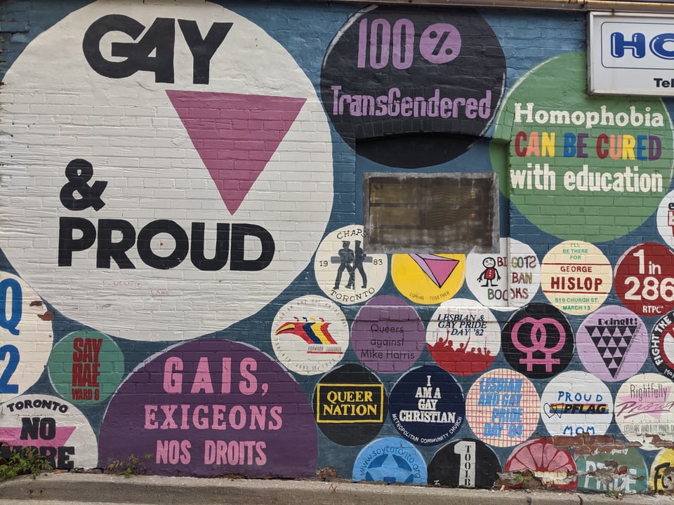 A brick wall painted with a ton of pictures of buttons with pro-LGBT slogans.