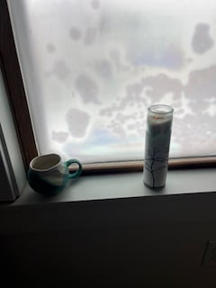 novena candle and ceramic teacup on the windowsill with fog and ice patchworking the glass