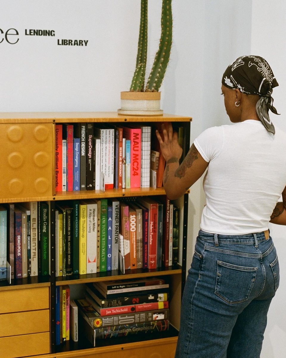 A person browsing big hardcover books on wooden bookselves.
