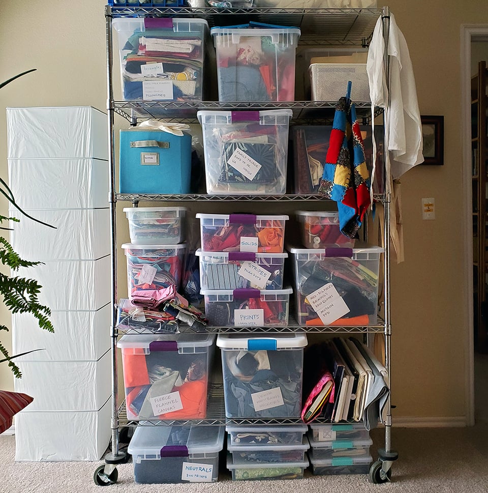 Photo of the shelving unit that houses Sarah's fabric stash. The shelves are filled with labelled bins of different types of fabric.