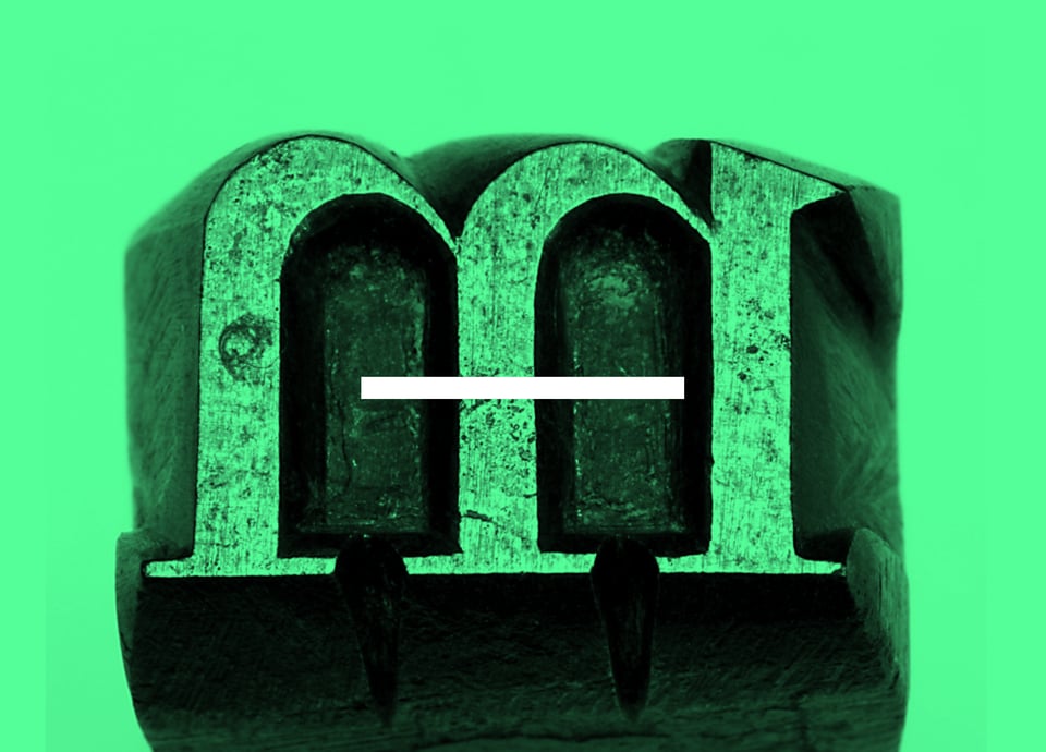 A close-up of a punch with the letter "m" and a horizontal line, set against a bright green background.