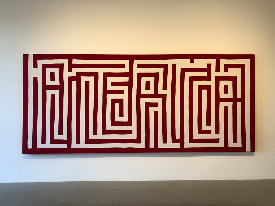 A horizontal painting on a wall consists of red and white quilted textile pieces that spell the word "America"