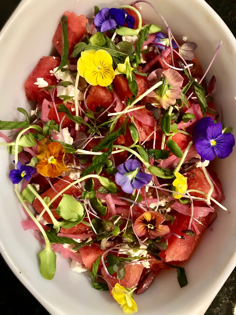 photo of a watermelon salad with a lot of sunflower greens and viola flowers on top.