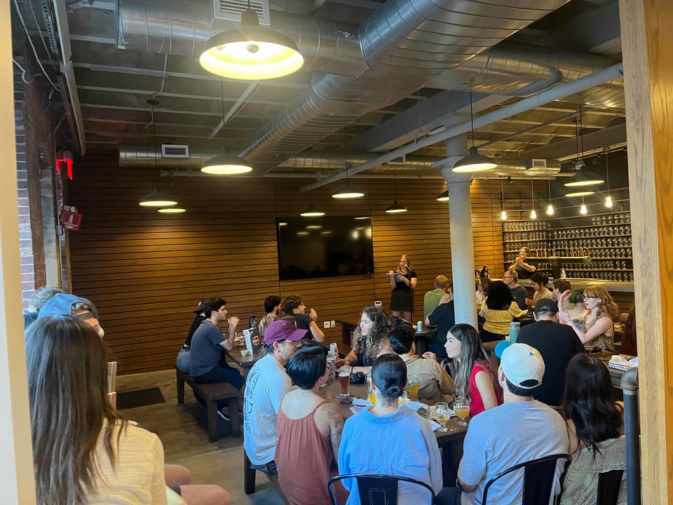 Amy at the mic hosting Slam Adams, a large crowd is present