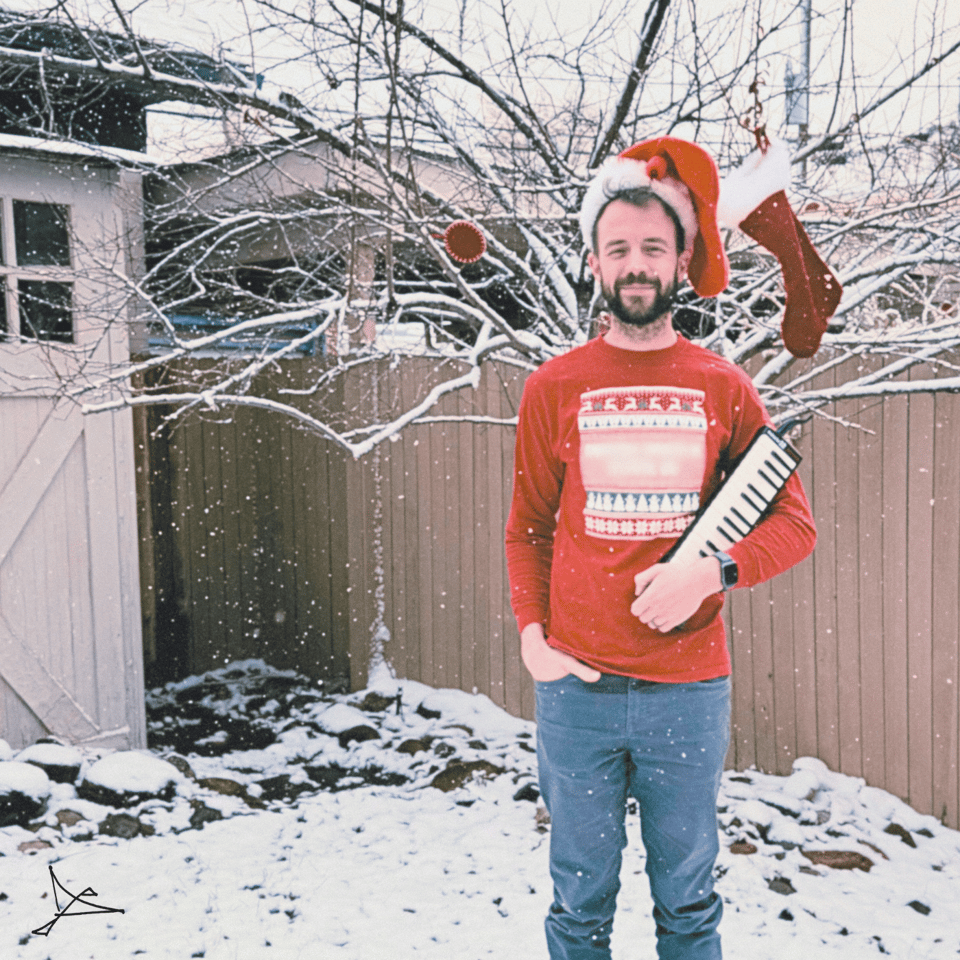 a man outside in the snow wearing a stocking on his head and holding a melodica, festive