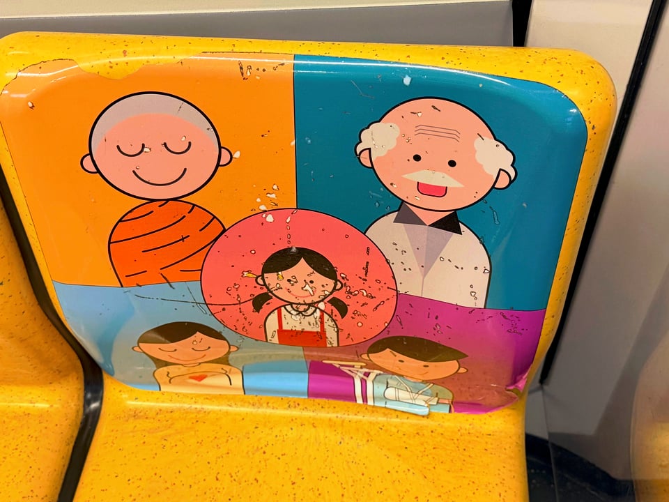 image of the priority seating on Bangkok metro, with friendly comical images of a monk, a child, an elderly person, a pregnant woman and an injured person