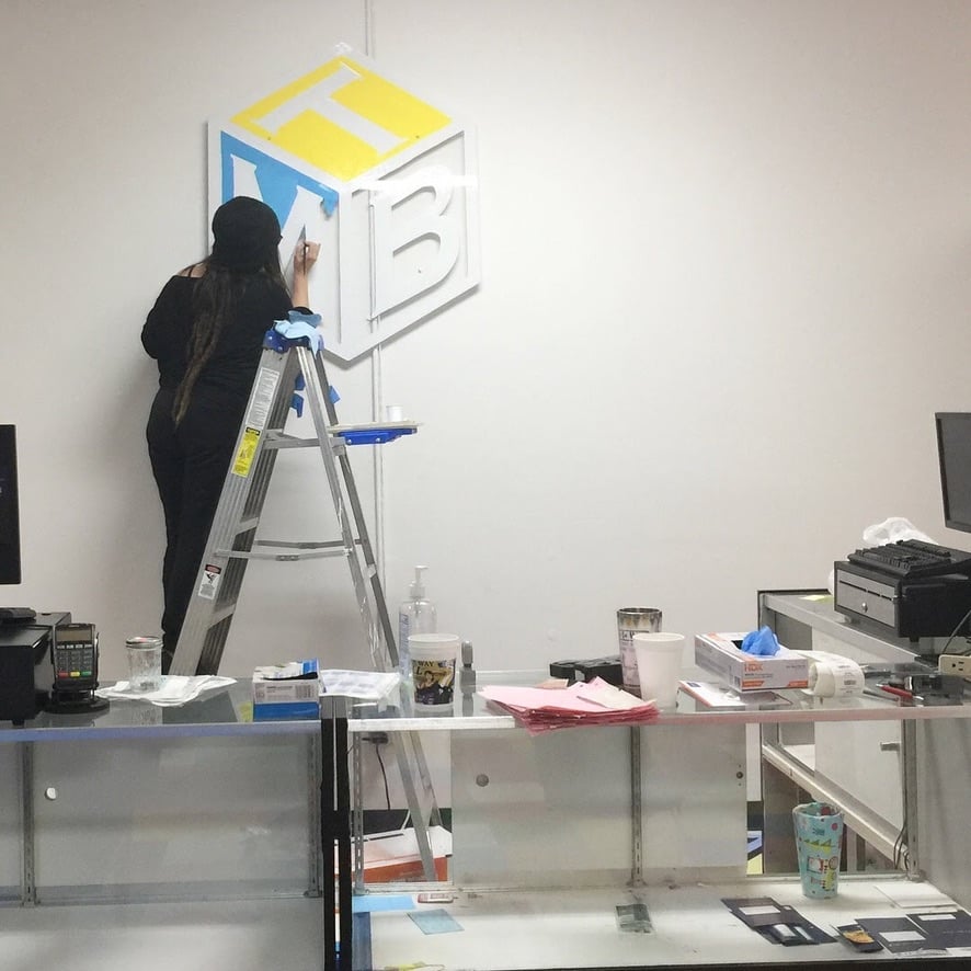 A person on a latter in a retail store painting a logo