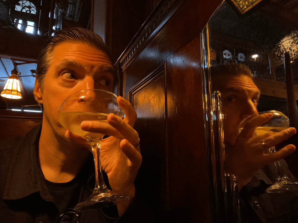 A person drinking a cocktail next to a mirror, startled by their reflection