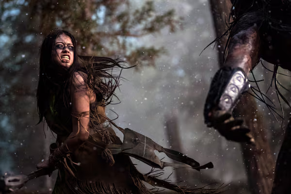 a film still of a north american plains warrior in the woods swinging an axe at an alien creature