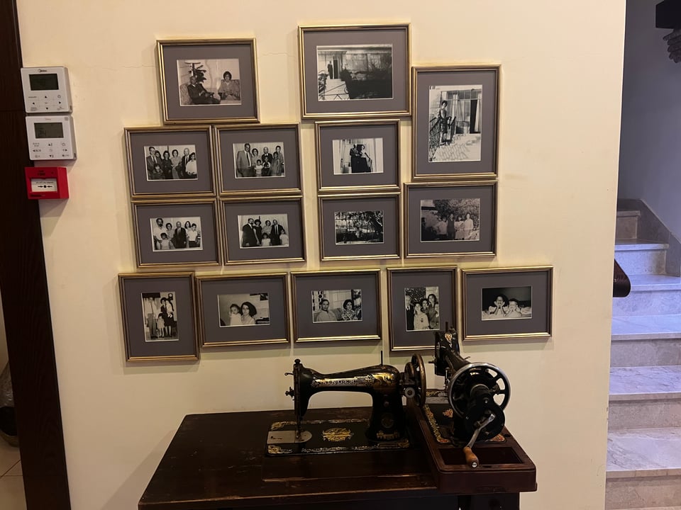 A wall with 15 black and white framed photographs, in front of two antique Singer sewing machines