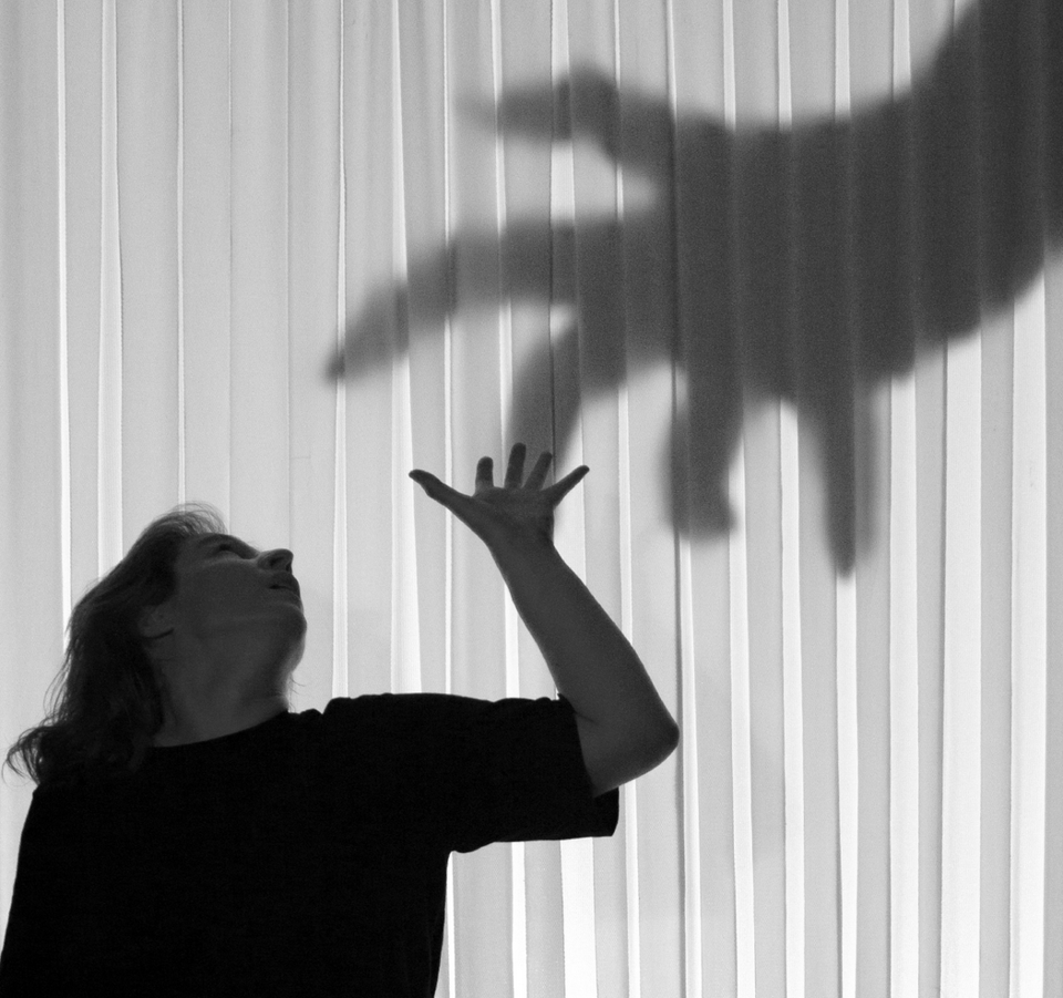 a woman standing in front of a screen a big shadow of a hand upon her