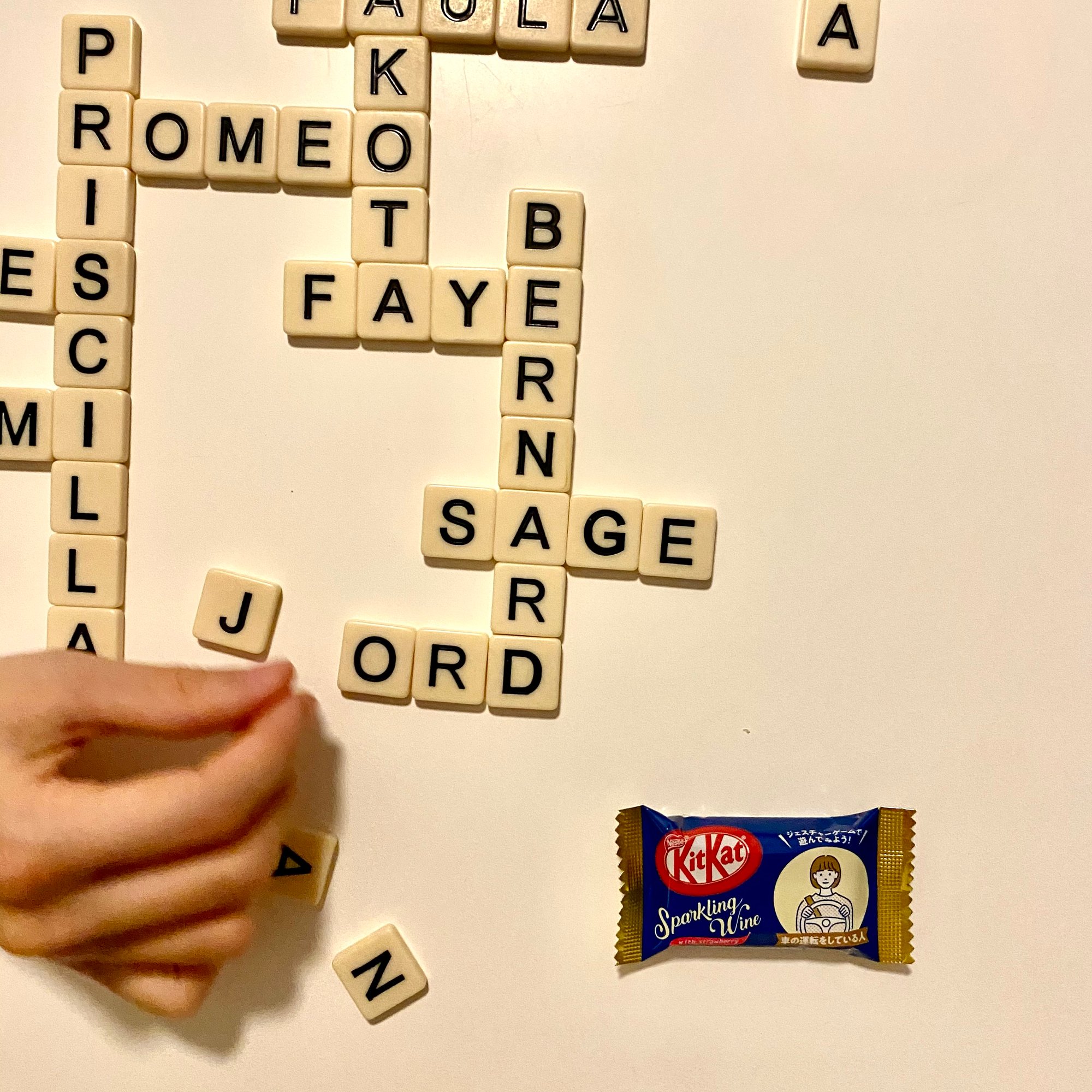 Photo of Bananagrams words on the table with a hand reaching on the left and a Sparkling Wine KitKat on the right.
