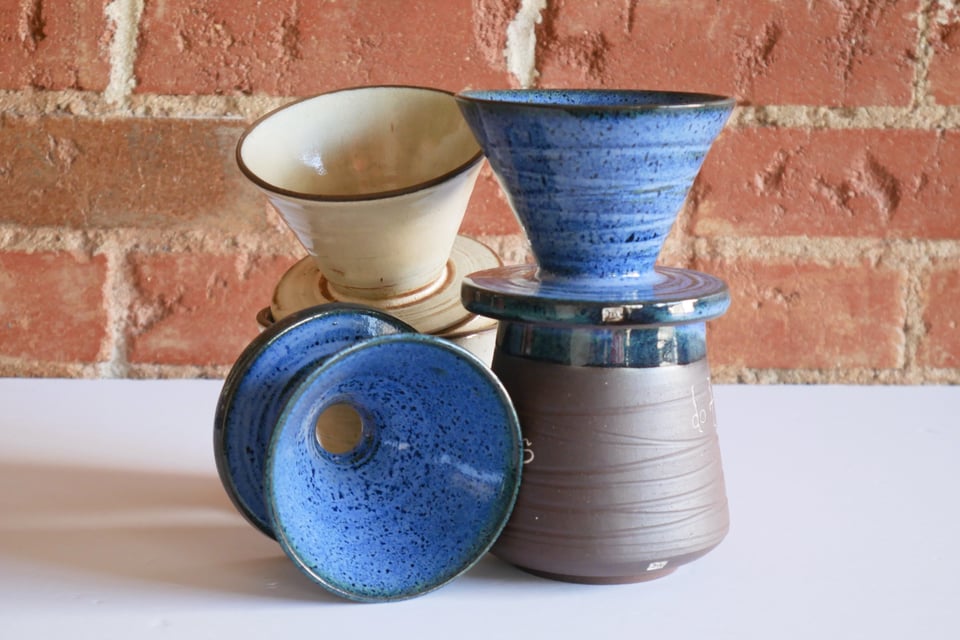 Inverted hollow cone shapes piercing a wide flat base that fits over one of the tumblers - for brewing pour-over coffee with a v60 filter