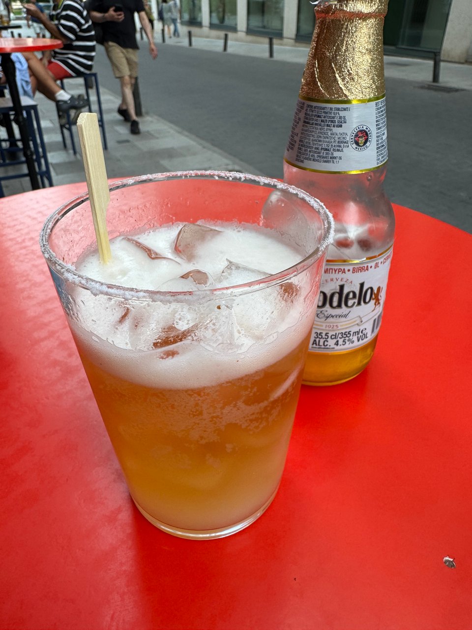Chelada beer with ice — glass of Modelo beer with ice and salt rim on a red table.