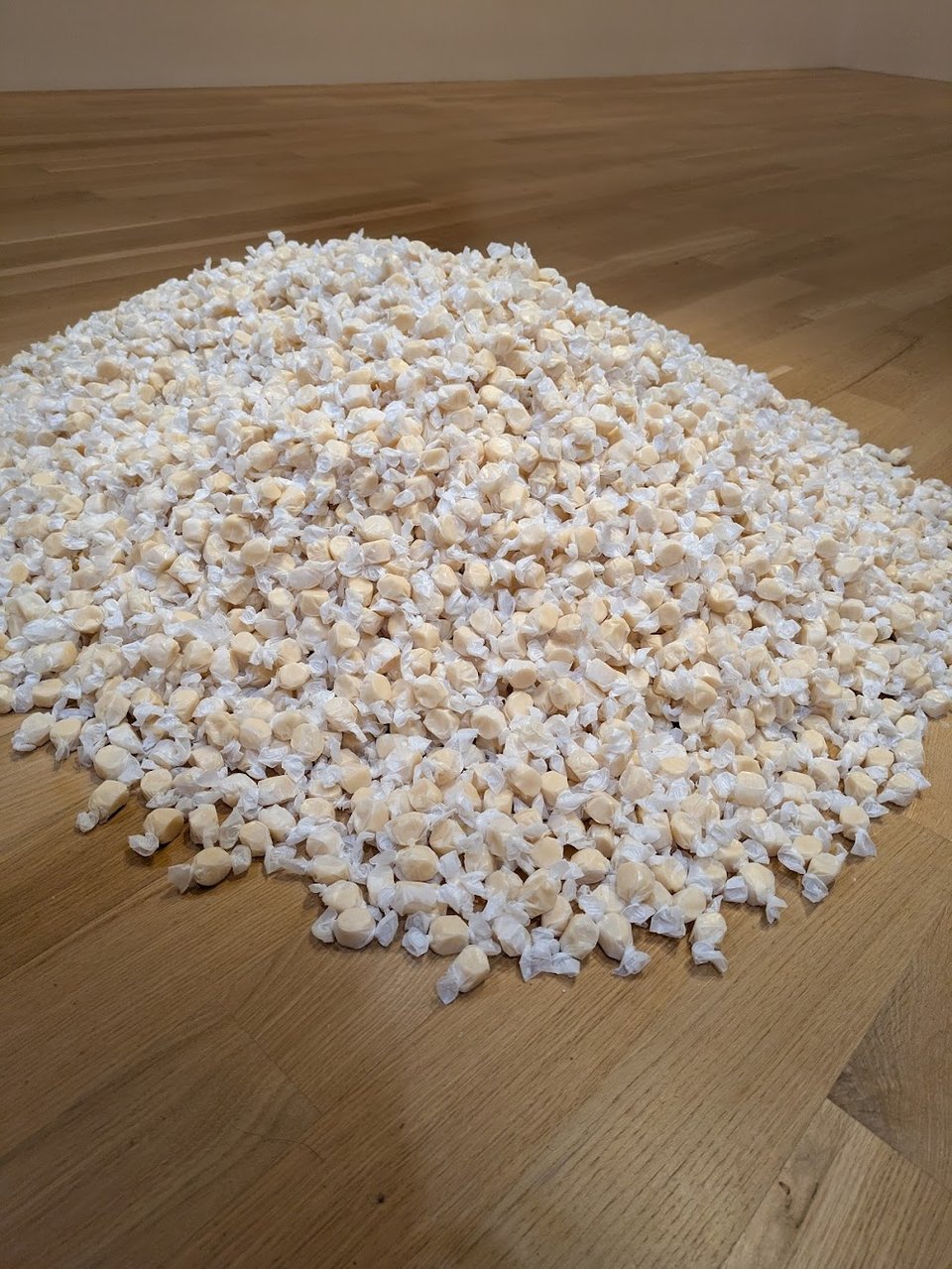 A pile of tan taffy-like candies on the floor, in translucent wax paper wrappers.