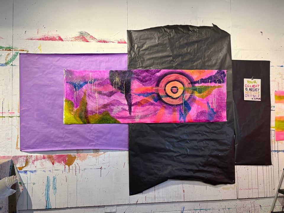 A photo of a painting tacked on a wall against a dark paper background to make it stand out. The painting includes several neon colors.