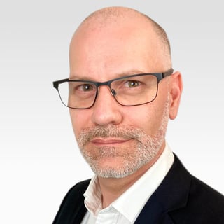 A white man with glasses, a salt and pepper beard. He's looking at you.