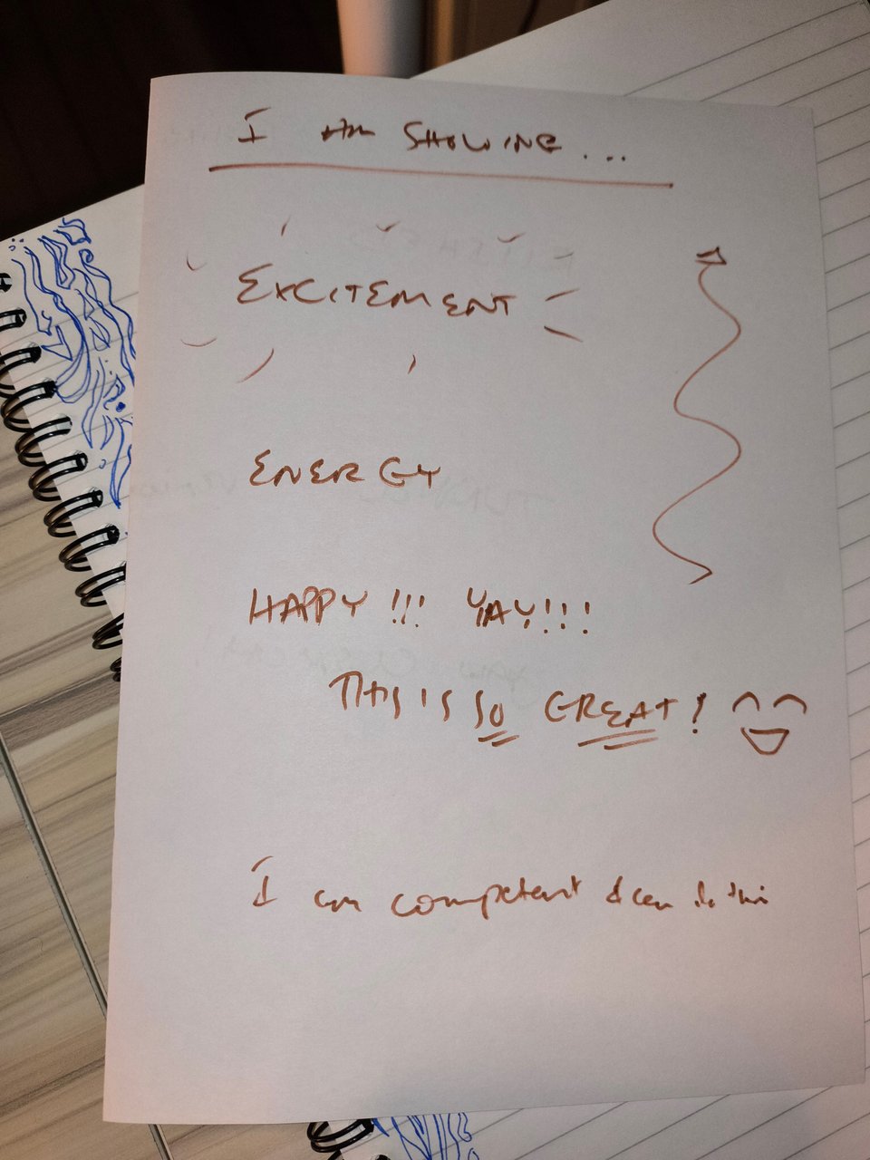 A page with some doodling in brown reading "EXCITEMENT! ENERGY! HAPPY!!! YAY!!! THIS IS SO GREAT! I am competent and can do this." with some jazzy smiley faces and up arrows on it.