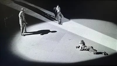 Still frame from The Long Wait featuring a bound woman crawling across the floor toward a bound man while a second man watches