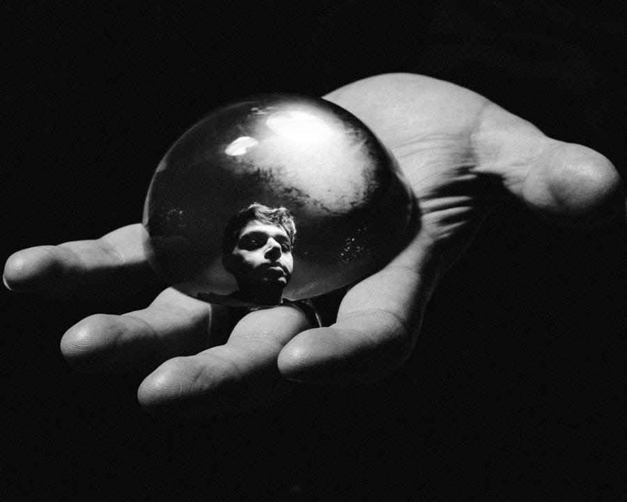 A open palm holds a reflective half-sphere that shows a man's face.