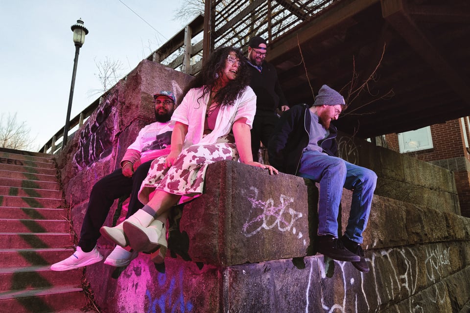 A woman and three men sit on the abuttment of an old railroad bridge at dusk.