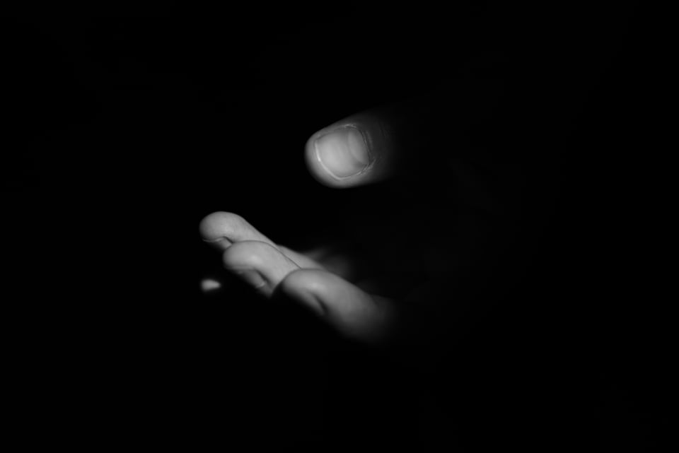 A photograph of a dimly lit hand beckoning ambiguously against a black background.