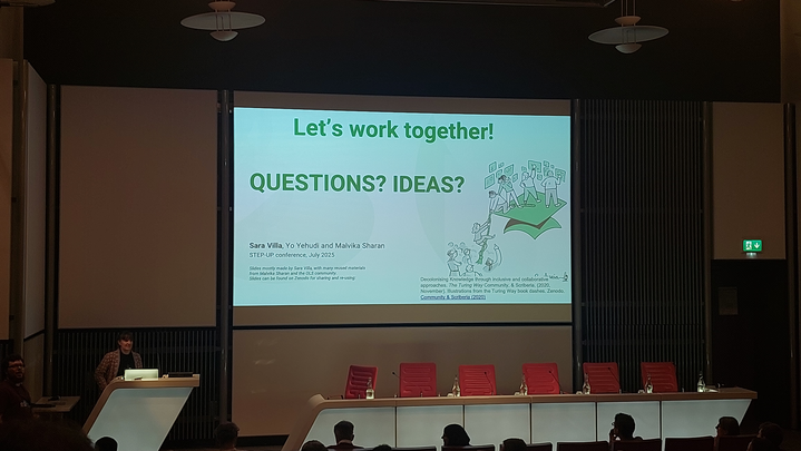 Sara presenting in a stand a slide on a big projector with a slide saying Let's work together, questions? ideas?