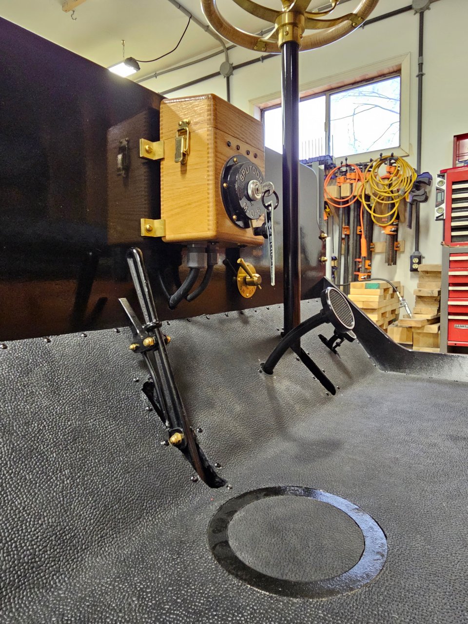 The dashboard featuring the steering wheel on a vertical column and a wooden box with brass hardware for the key