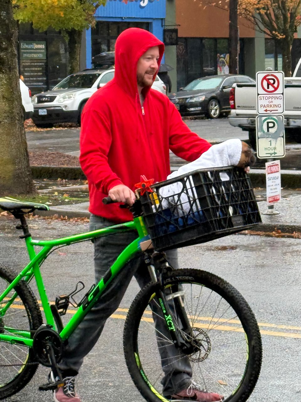 A man dressed in a red hoodie pushes a bike. In the bike's basket is a dog wrapped in a blanket. They're dressed as ET and Eliot