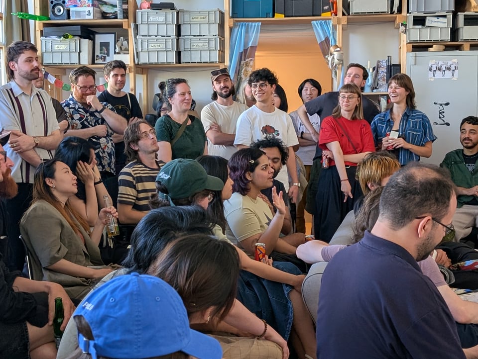 A variety of gestures and reactions across a crowded room. The mood is boisterous and amused.