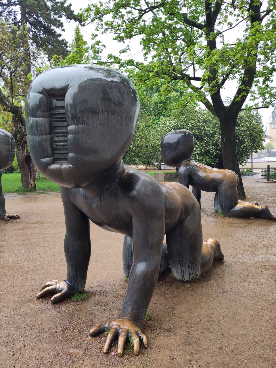Statue eines krabbelnden Babys, dessen Gesicht von einem eingestanzten Strichcode ersetzt ist.. Im Hintergrund weitere Babys. Es handelt sich um eine bekannte Plastiken-Serie von David Černý.
