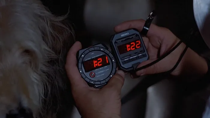 Marty holds up a digital stopwatch and a digital watch, each reading different times (1:21 and 1:22)