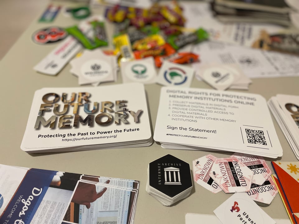 A table full of cards and stickers, including postcard for "Our Future Memory" and the Internet Archive.