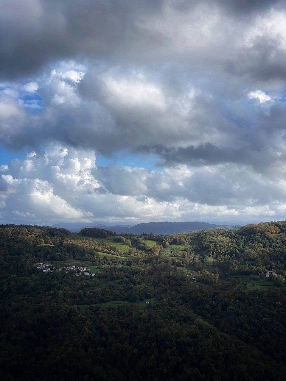 A view of rural Slovenia. Cloudy sky, green fields and a few houses.