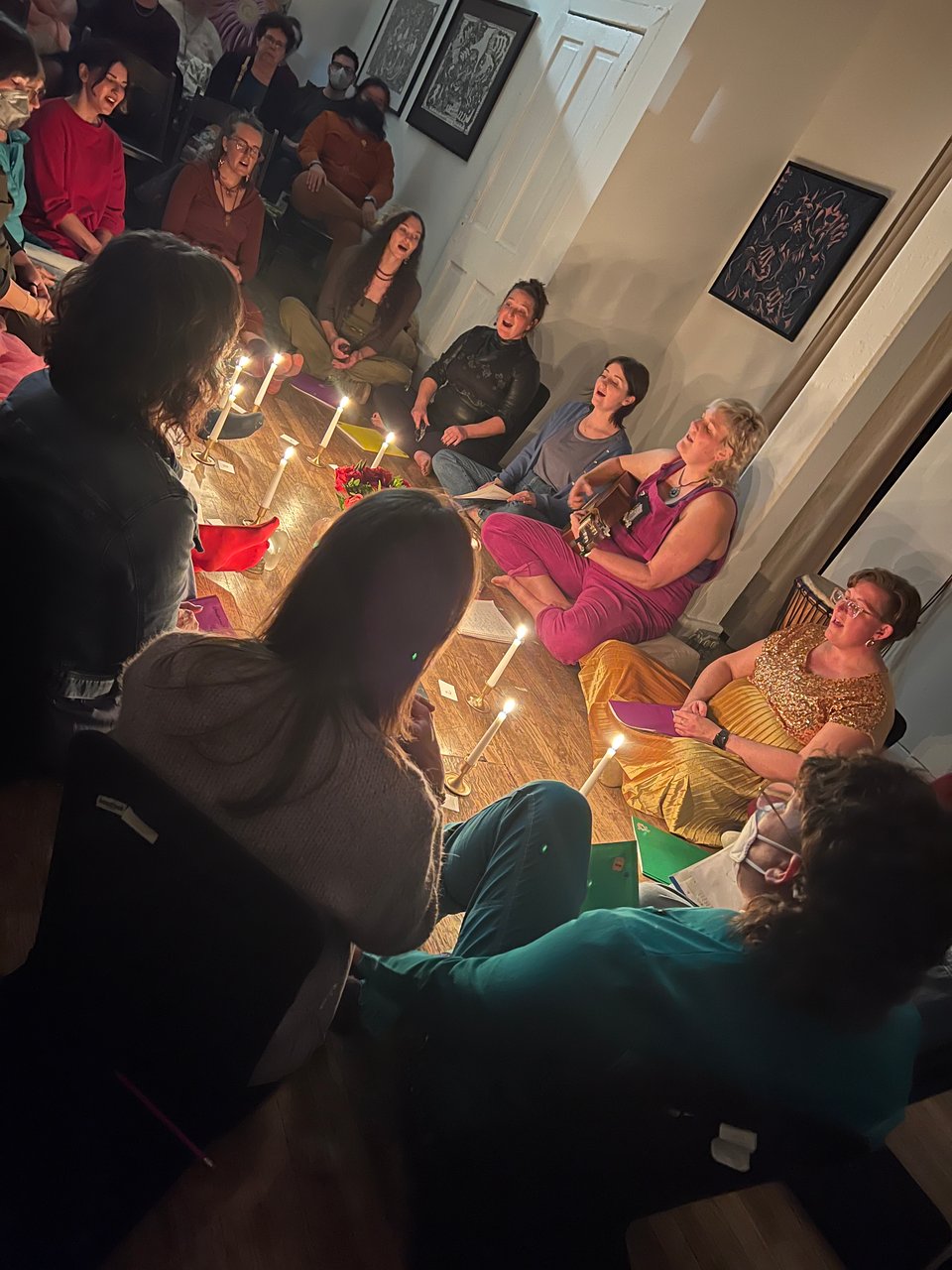 A group of people sitting in a circle singing by candlelight