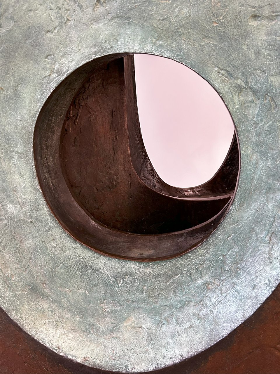 A close up photo of a bronze Hepworth statue. The form is made up of two smooth curved stones that have been pieced. The piercings are organic and differently angled, so that looking through it - like in this photo - layers are revealed.