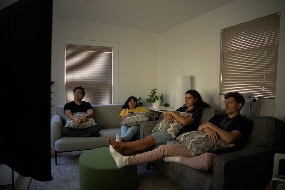 A group of people sitting on a couch watching a TV.