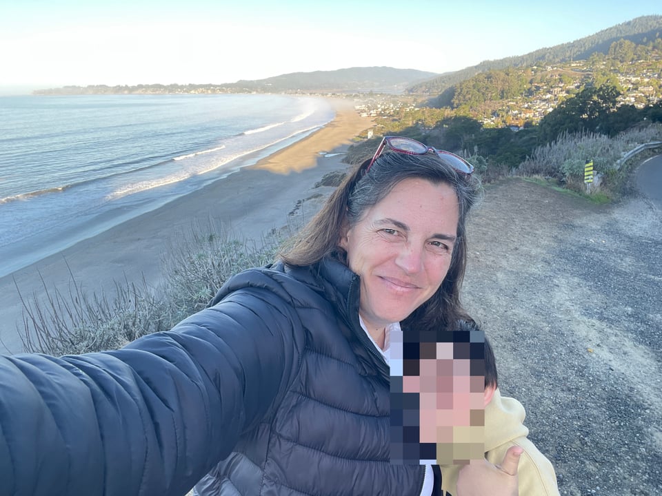 Woman and child stand in front of Stinson Beach and Bolinas in the background. Child's face is blurred.