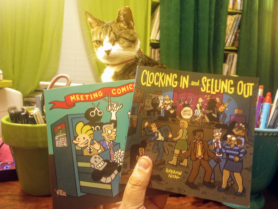 My hand holding my two books and my cat Tip in the background