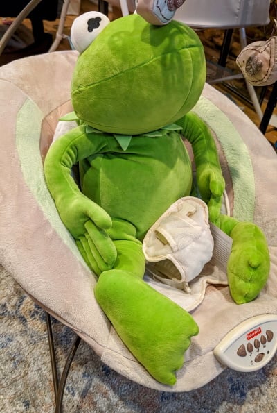 a giant stuffed Kermit the Frog in a baby chair