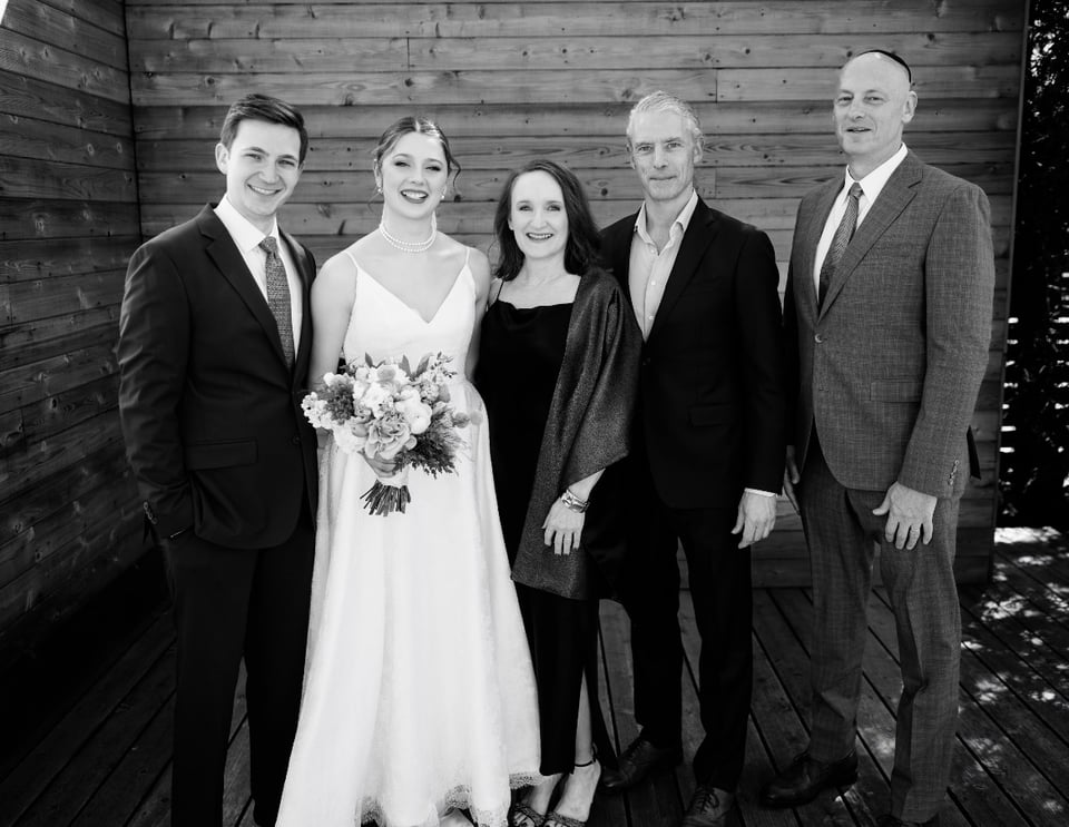 B/W photo at wedding: l-r: groom, bride, aunt, uncle, father of the bride. The uncle hasn’t put his tie on yet, so thus looks louche. The aunt is in 4” heels and is still by far the shortest person in the picture. The bride looks beautiful