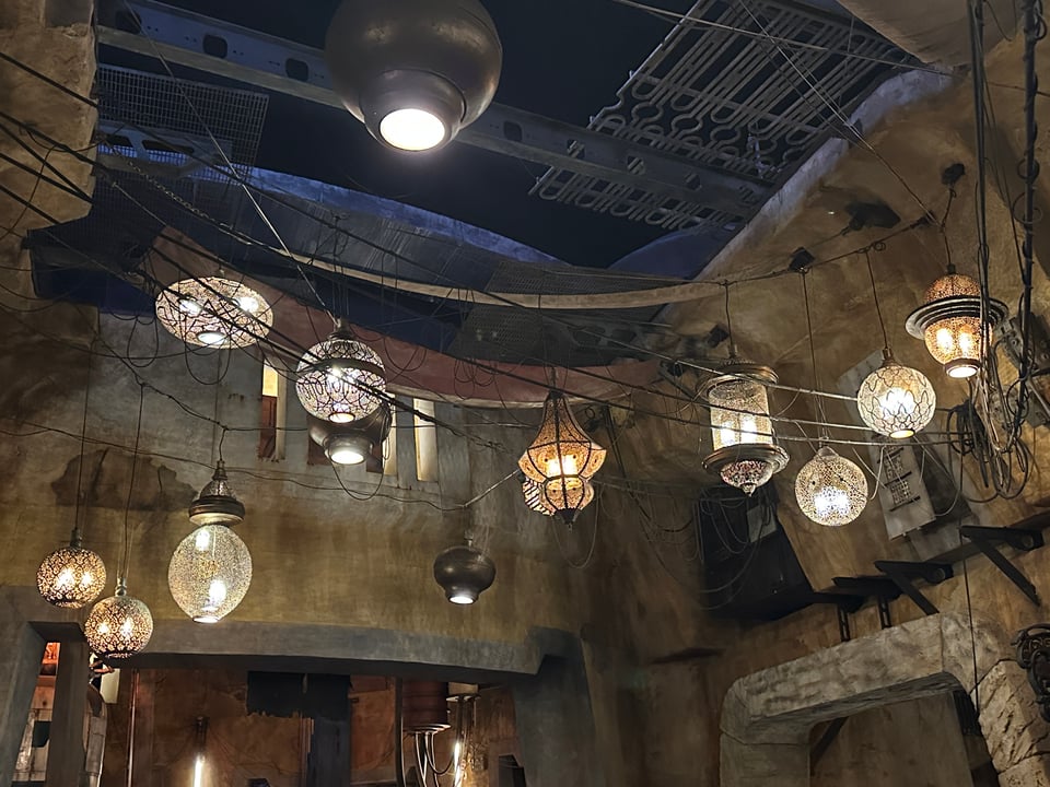 The Marketplace in Black Spire Outpost in Star Wars: Galaxy's Edge in Disney's Hollywood Studios, at night: rough-rock buildings lit by haphazardly strung golden lanterns.