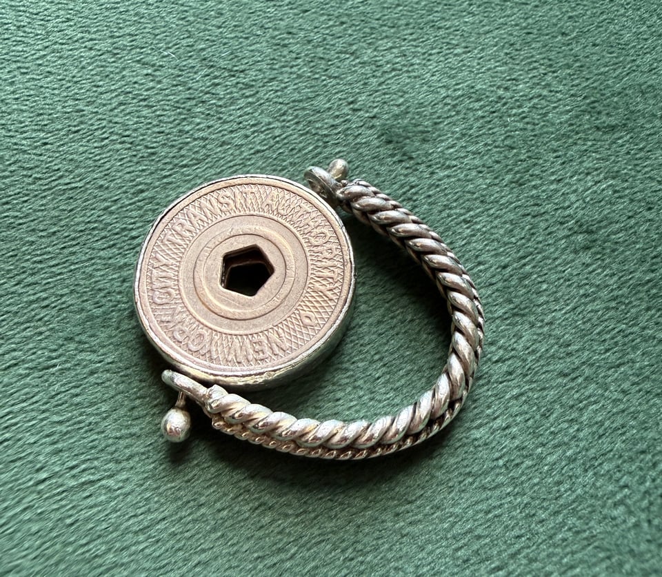 NYC subway token set in a braided silver ring against green background