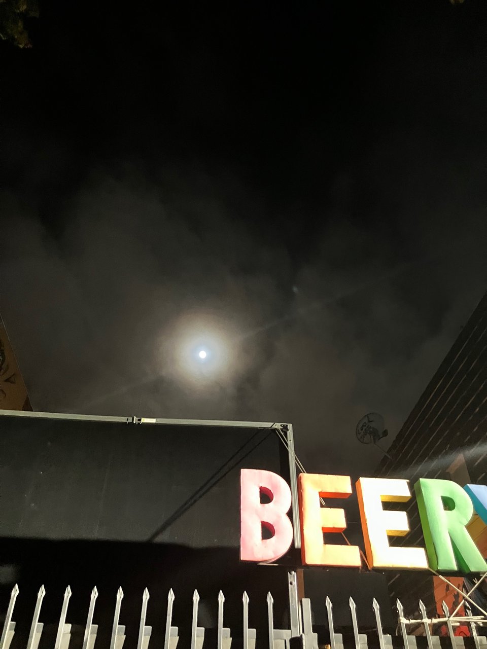 A full moon in the dark sky above Beeryland (Telegraph Beer Garden) in Oakland, California.