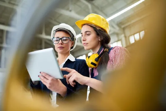 two women in hard hats looking at a tablet